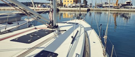 A marina with multiple sailboats docked, a building in the background, and calm water.