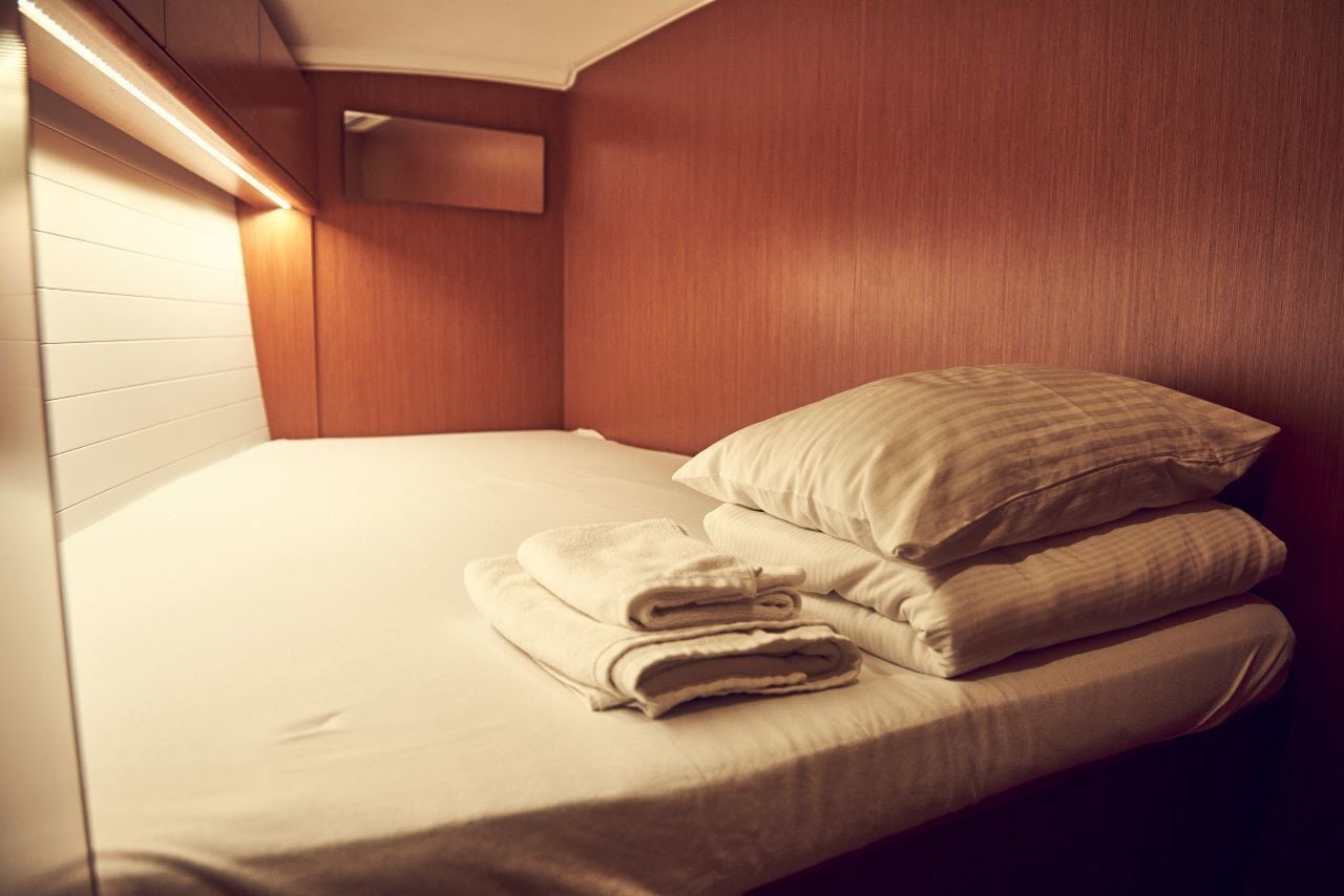 A single bed with a headboard, a wall-mounted light, and a small window.