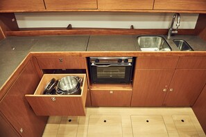 A compact kitchen with wooden cabinets, a built-in oven, a sink, and a drawer with cookware. - Sun-Kissed Sailing Adventure in Istria, Croatia (Pula)