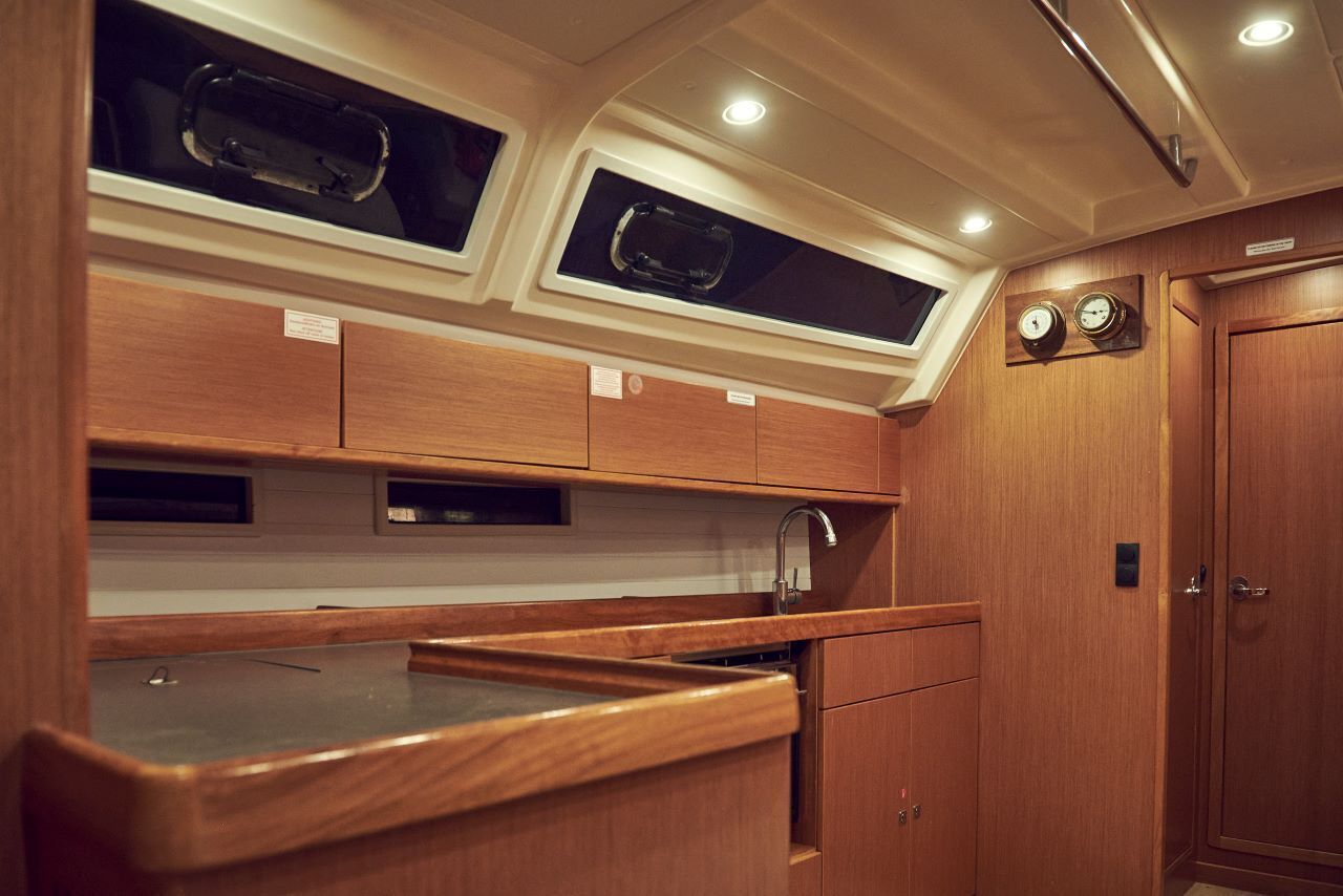 A compact kitchen with wooden cabinetry, a sink, and two windows above the countertop.