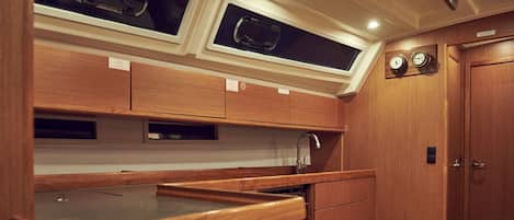 Cocina compacta con armarios de madera, un lavamanos y dos ventanas sobre la encimera.