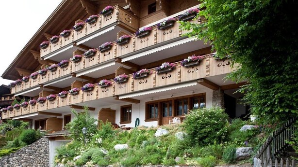 Ein mehrgeschossiges Gebäude mit Balkonen, die mit Blumen geschmückt sind, einer Steinsäule und einem Holzzaun.