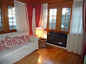 Ein gemütliches Wohnzimmer mit einem weißen Sofa, einem Flachbildfernseher und Holzböden.