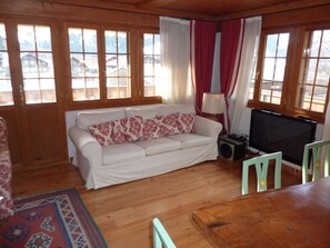 Ein gemütliches Zimmer mit einem weißen Sofa, einem Fernseher und einem Holztisch.