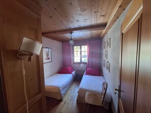 Ein Zimmer mit zwei Einzelbetten, einem fenster mit Vorhängen, einer Lampe und einer Gitarre.