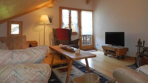 Ein gemütliches Wohnzimmer mit einer Couch, einem Tisch, einem Fernseher und einem Sessel.