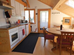 A kitchen with white cabinets, a stove, and a dining area with a round table and chairs. - Im Wiesengrund Appartement/Fewo, Dusche oder Bad, WC 4-Bettwohnung by Interhome (Gstaad)