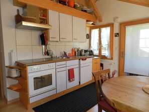 A kitchen with white cabinets, a wooden countertop, a stove, and a dining area with a table and chairs. - Im Wiesengrund Appartement/Fewo, Dusche oder Bad, WC 4-Bettwohnung by Interhome (Gstaad)