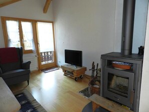 A living room with a sofa, a television on a wooden stand, a fireplace, and a sliding glass door leading to an outdoor area. - Im Wiesengrund Appartement/Fewo, Dusche oder Bad, WC 4-Bettwohnung by Interhome (Gstaad)