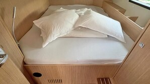 En lille seng med hvide sengetøj i en hytte med trævægge og et vindue.