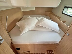 Ein kleines Bett mit weißer Bettwäsche in einer Holzhütte mit einem Fenster.