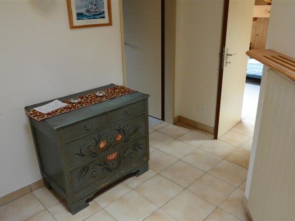 A room with a dresser against a wall, a door leading to another room, and a tiled floor. - Mireille Nr. 8 Appartement/Fewo, Dusche oder Bad, WC 6-Bettwohnung by Interhome (Gstaad)