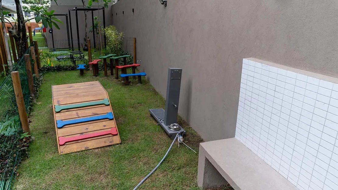Un espacio exterior cercado con un parque infantil de madera, un banco de metal y un muro de baldosas.