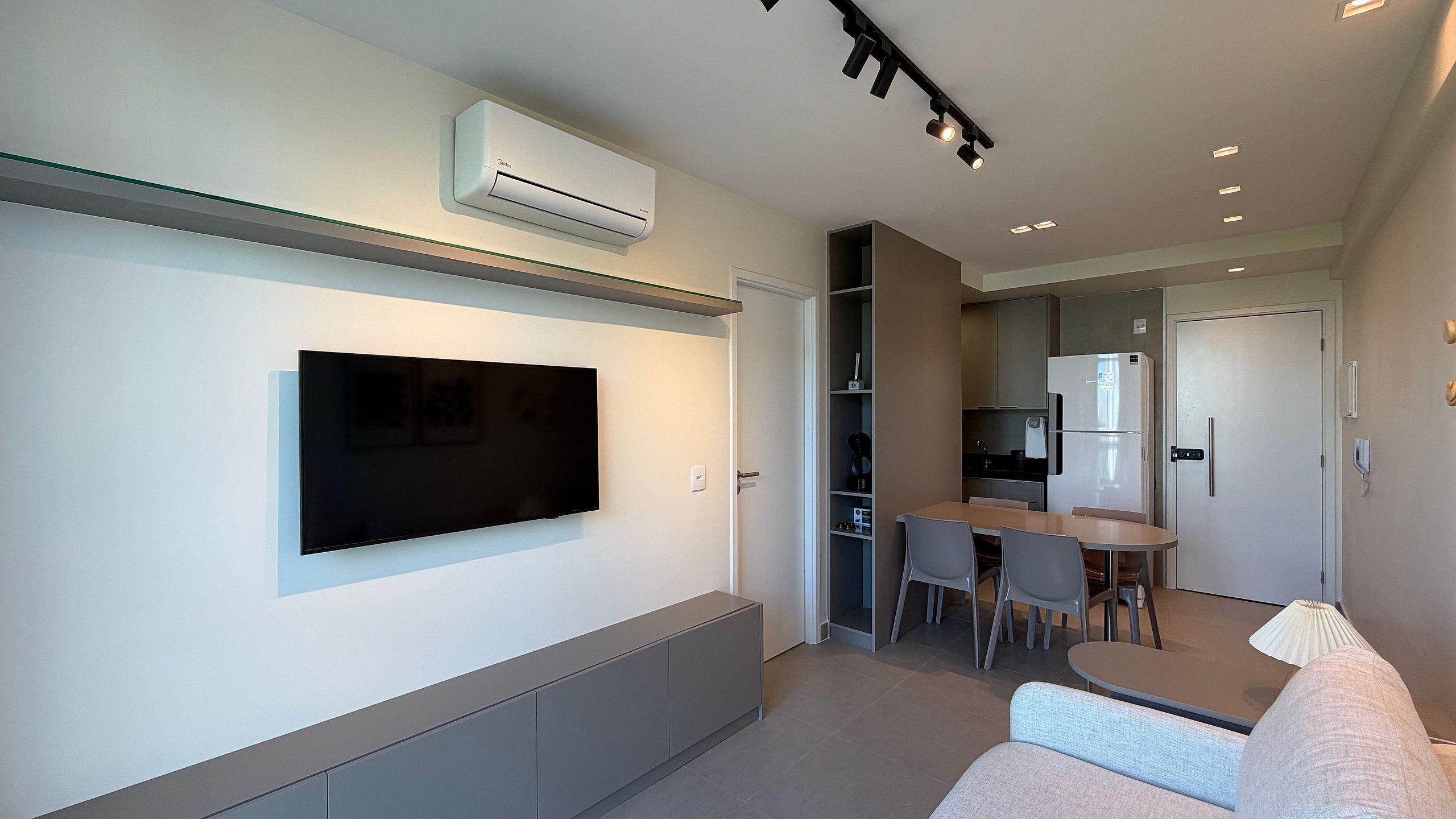 Una sala de estar moderna con un televisor de pantalla plana montado en la pared, un sofá gris y un comedor con mesa y sillas.