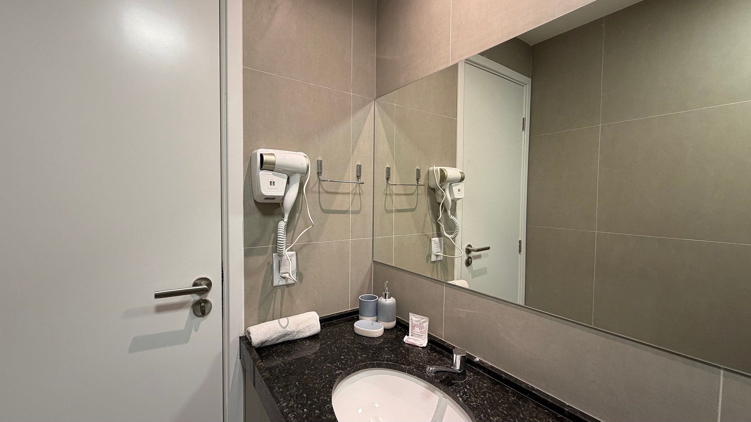 A bathroom with a white sink, a mirror, and two hair dryers mounted on the wall.