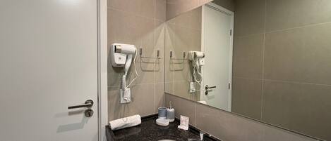 A bathroom with a white sink, a mirror, and two hair dryers mounted on the wall.