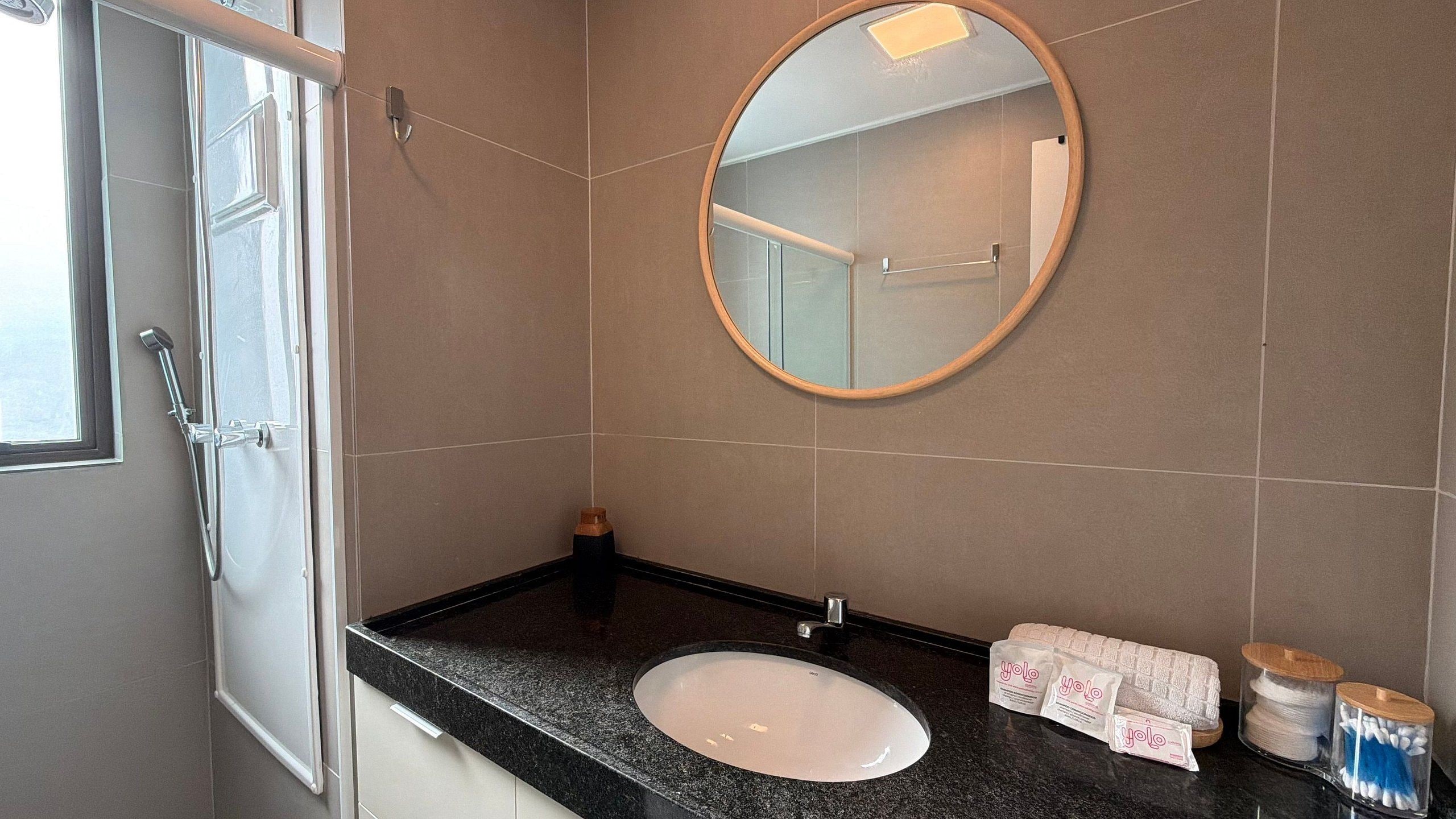 Un baño con un lavabo blanco, un espejo redondo y artículos de aseo en la encimera.