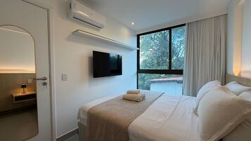 Una habitación de hotel con cama, televisor montado en la pared, ventana con cortinas y aire acondicionado.