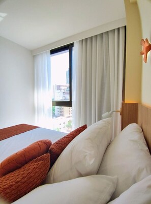 A hotel room with a bed, a window with curtains, and a view of buildings outside. - Casa Forte Prince por Yolo (Recife)