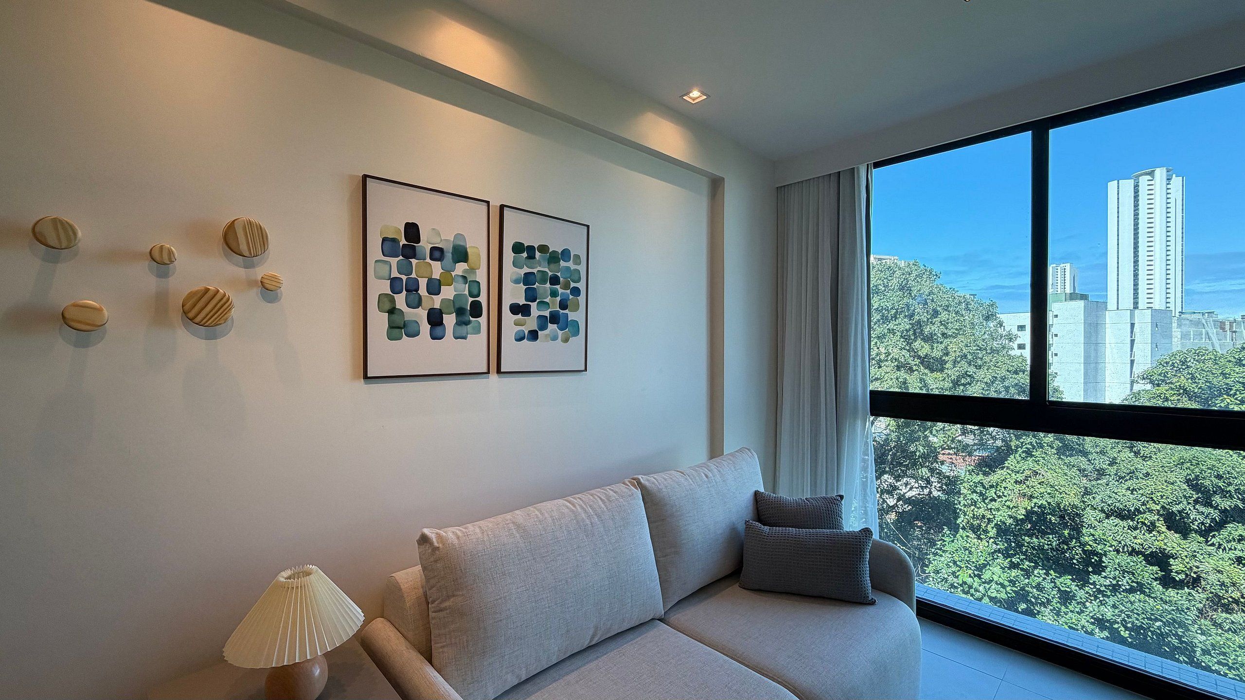 Ein modernes Wohnzimmer mit einem großen Fenster, einer Couch, dekorativen Kissen und zwei gerahmten abstrakten Kunstwerken an der Wand.