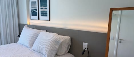 A hotel room with a bed, two pillows, a bedside table, a lamp, and a door.