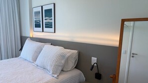 A hotel room with a bed, two pillows, a bedside table, a lamp, and a door.