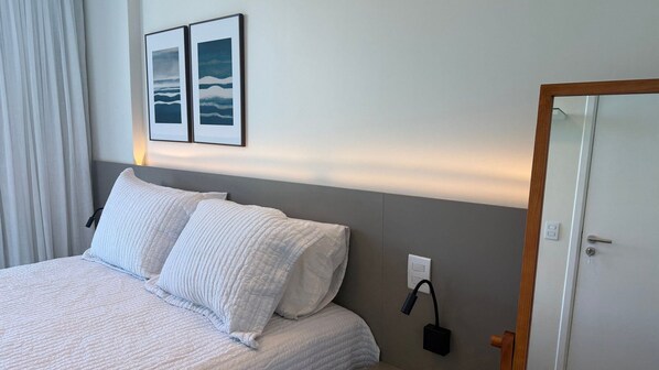 A hotel room with a bed, two pillows, a bedside table, a lamp, and a door.