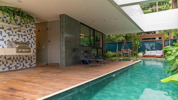 A modern outdoor pool area with a built-in grill, lounge chairs, and a hanging chair.
