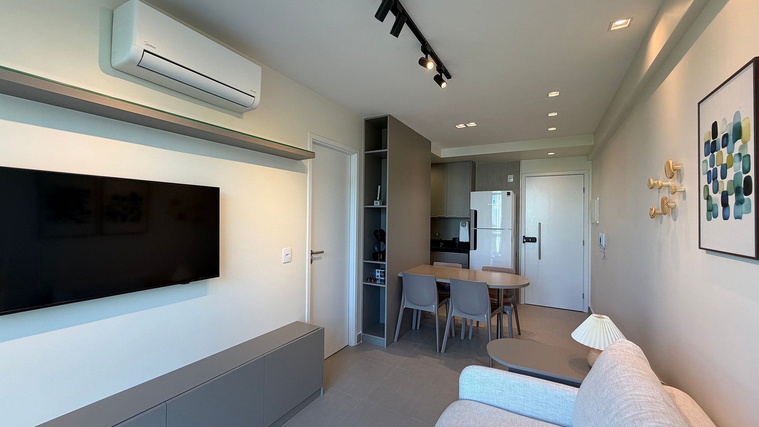 Uma sala de estar moderna com uma televisão de tela plana, um sofá e um espaço de jantar com cadeiras e uma mesa.