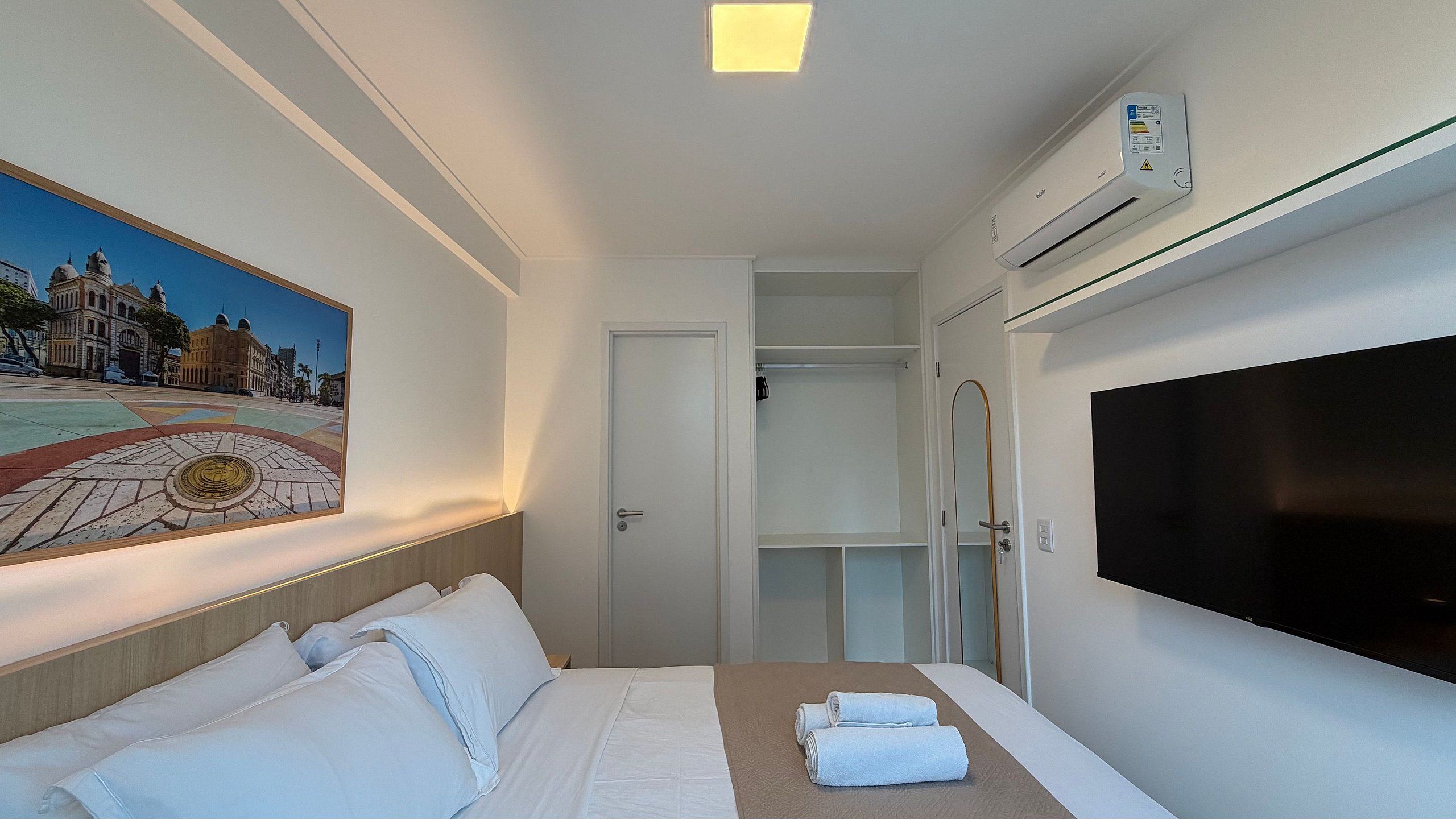 Habitación de hotel con cama, un cuadro, unidad de aire acondicionado, televisor y zona de ducha.