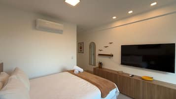A hotel room with a bed, a TV, a wooden dresser, and a wall-mounted air conditioner.
