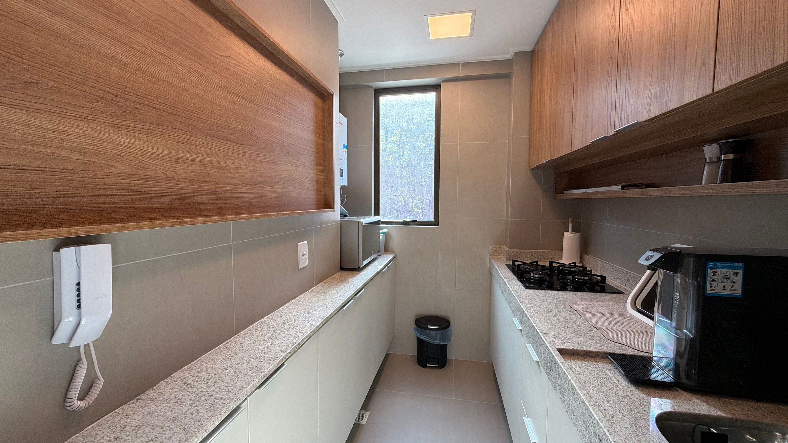 Una cocina estrecha con armarios de madera, una ventana y un bote de basura.