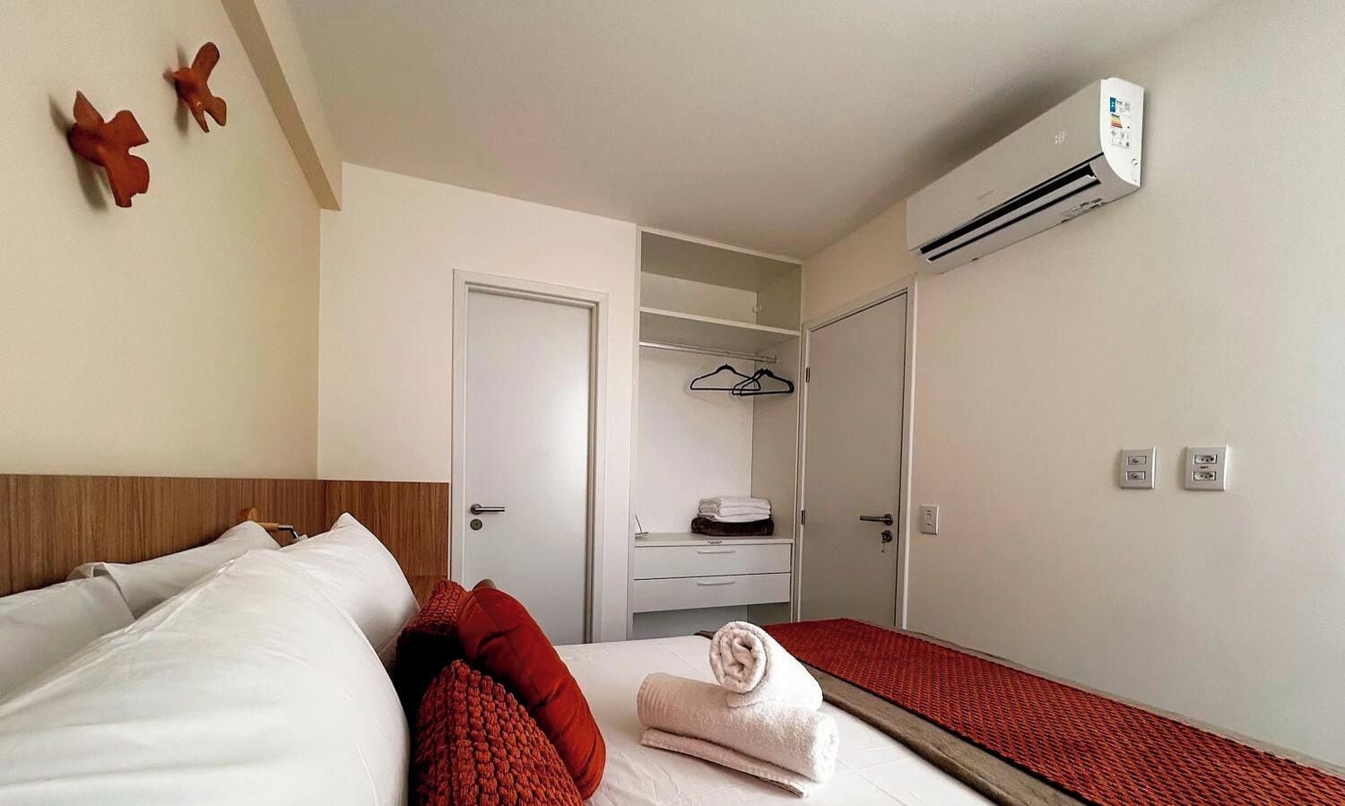 Habitación de hotel con cama, armario, espejo, equipo de aire acondicionado y alfombra roja.