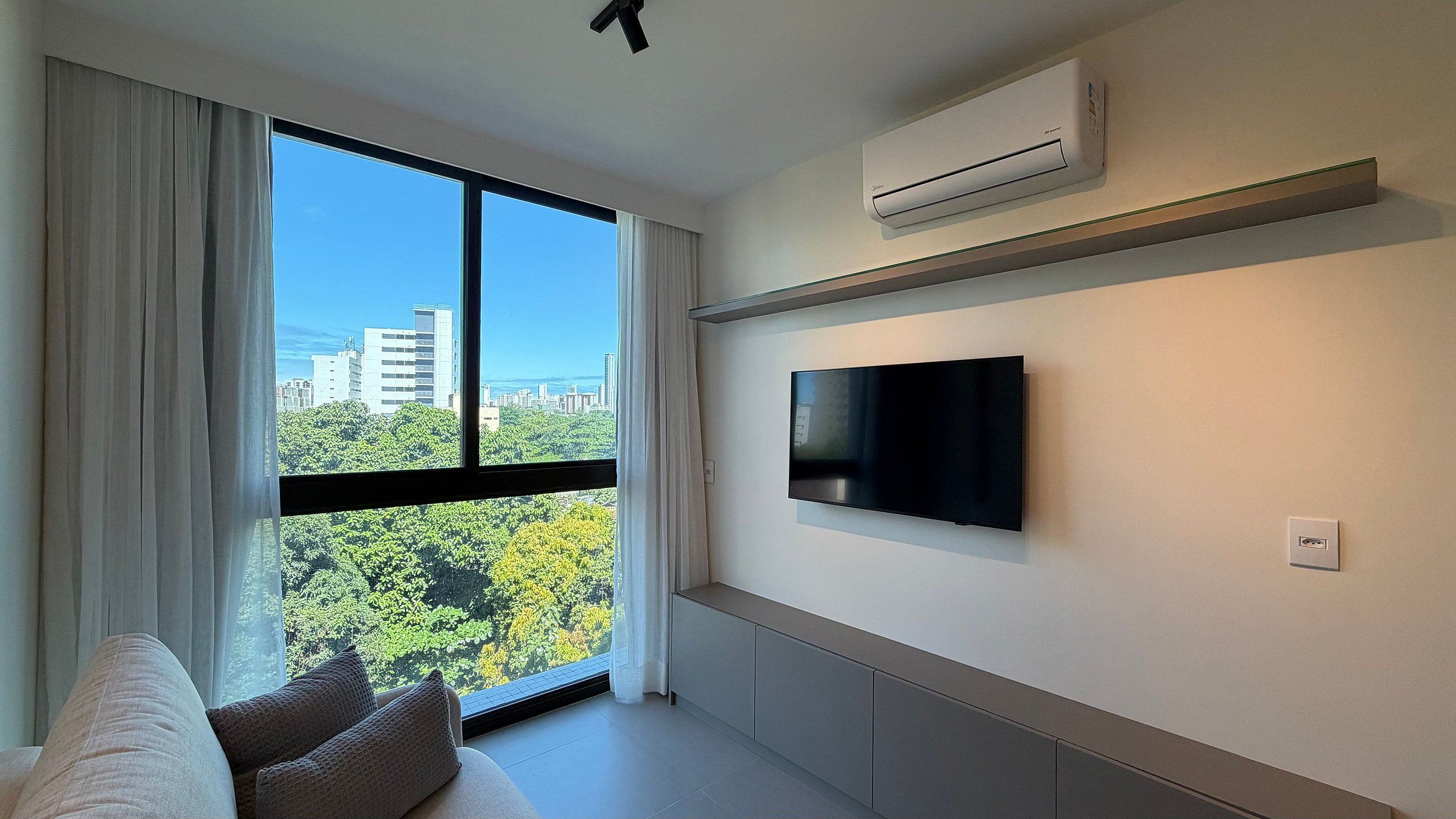 Ein modernes Wohnzimmer mit großem Fenster, einem an der Wand befestigten Flachbildfernseher und einer Couch.