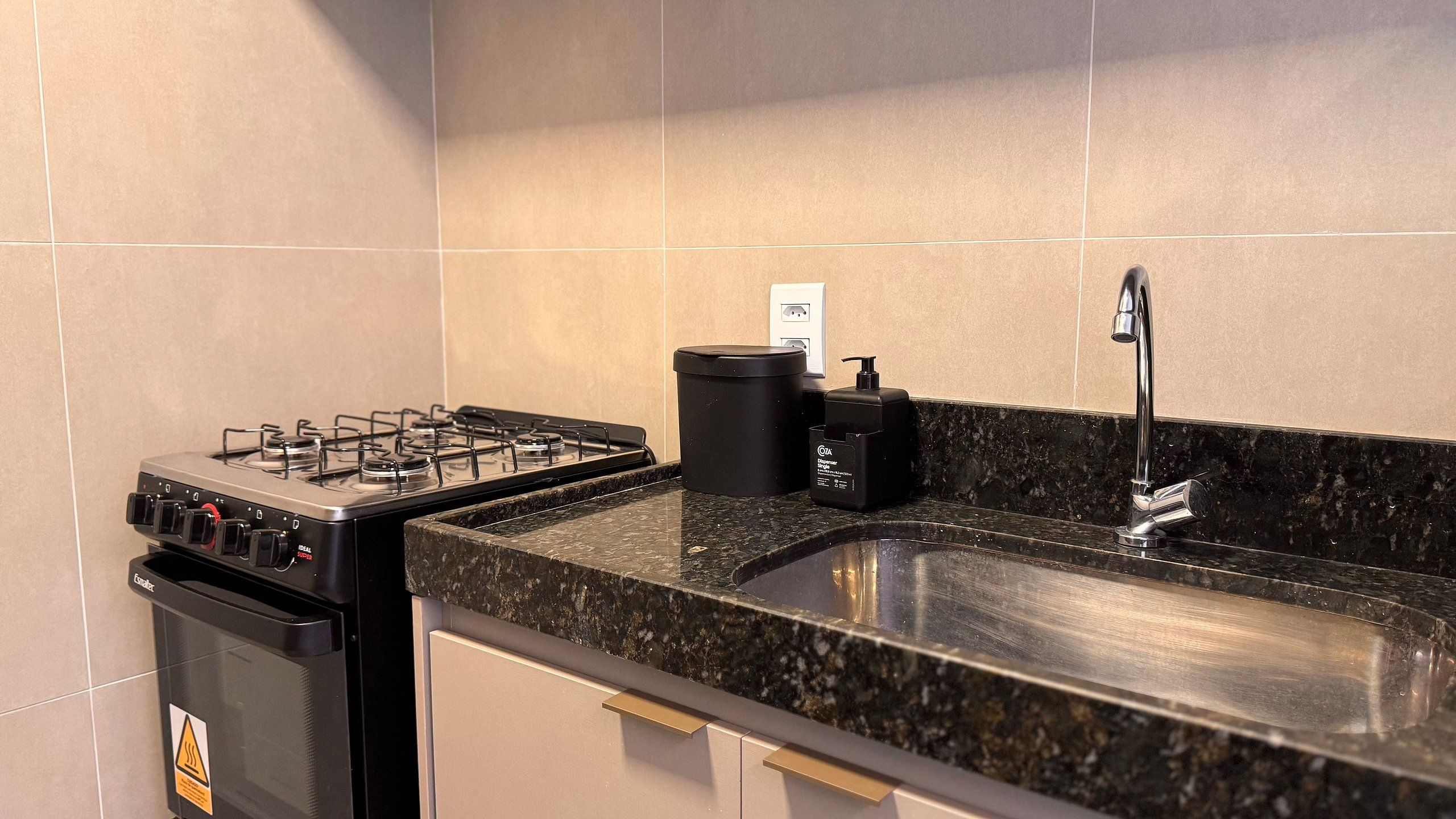 Una cocina con estufa a gas, un lavamanos y un cubo de basura.
