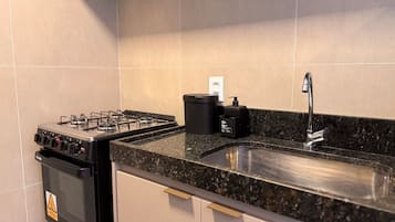 Uma cozinha com fogão a gás, pia e lixeira.