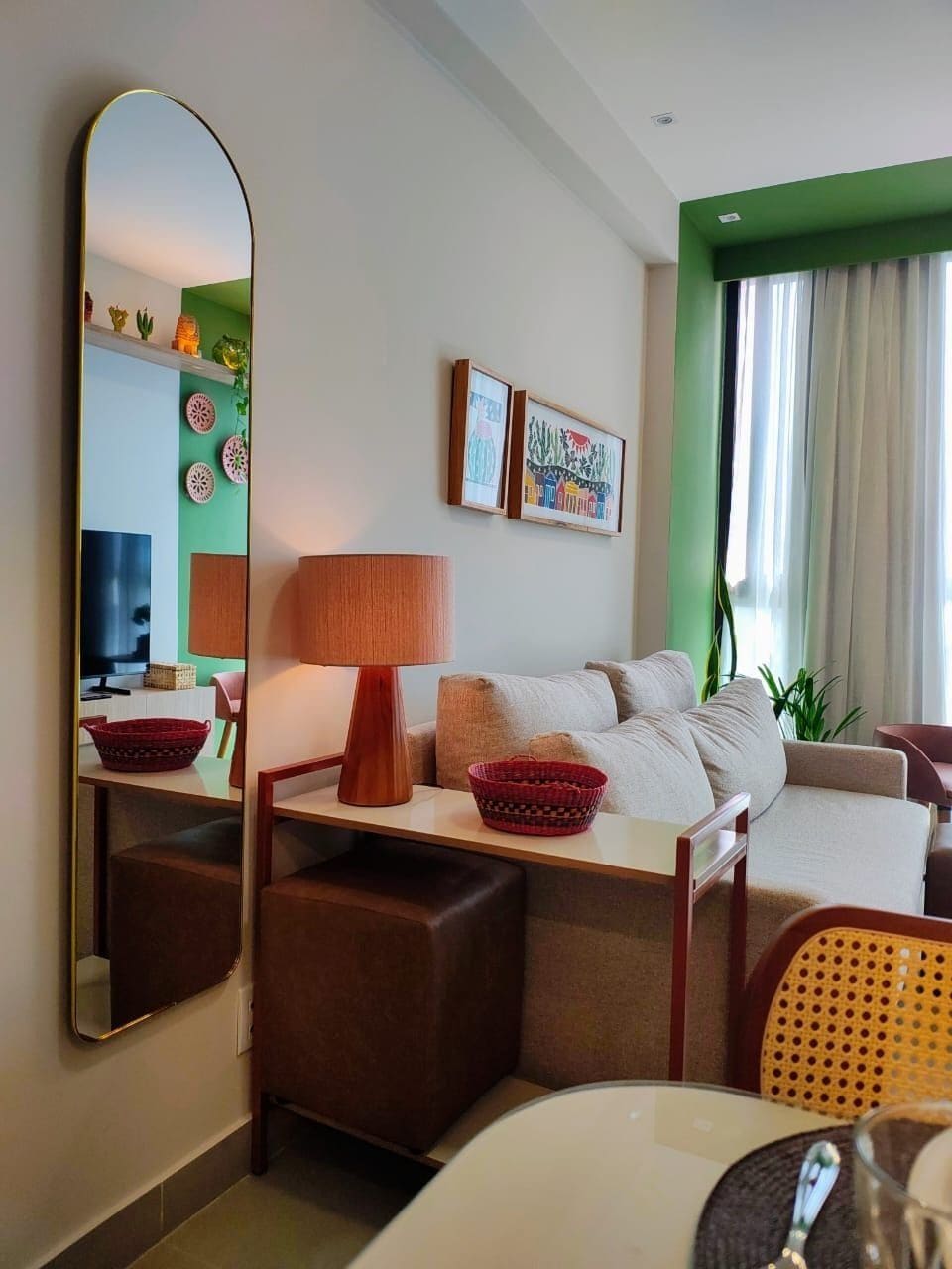 Una habitación de hotel con sofá, una mesa, lámpara, espejo y televisión.