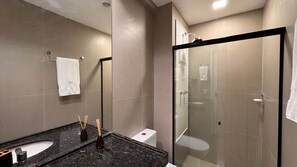Un baño moderno con ducha envuelta en vidrio, lavamanos de mármol negro y un inodoro blanco.