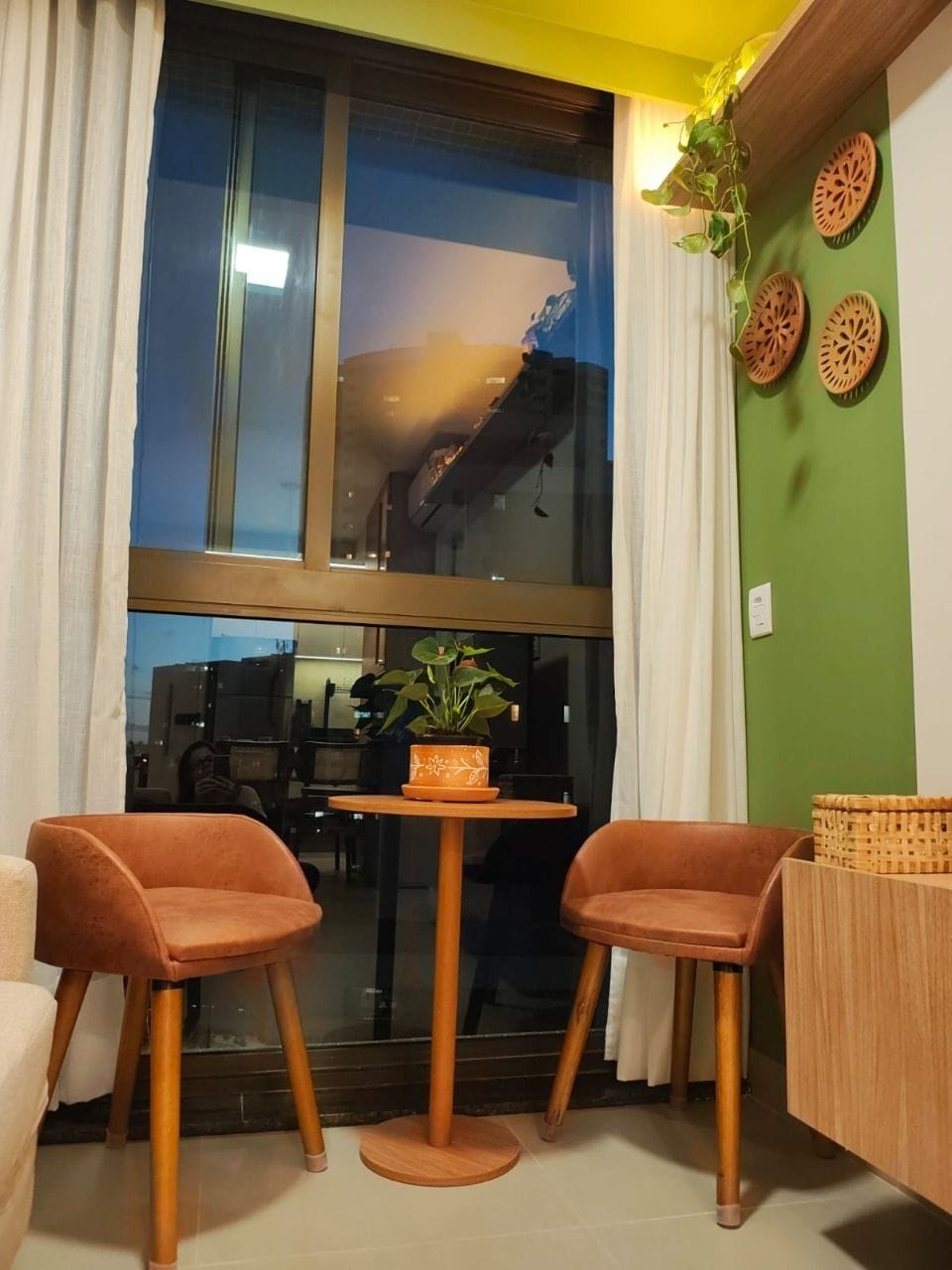 A room with a large window, two chairs, a small table, a potted plant, and decorative wall plates.