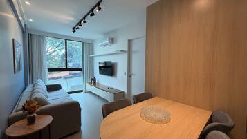 Una sala de estar moderna con un sofá, una mesa de comedor y un televisor montado en la pared.