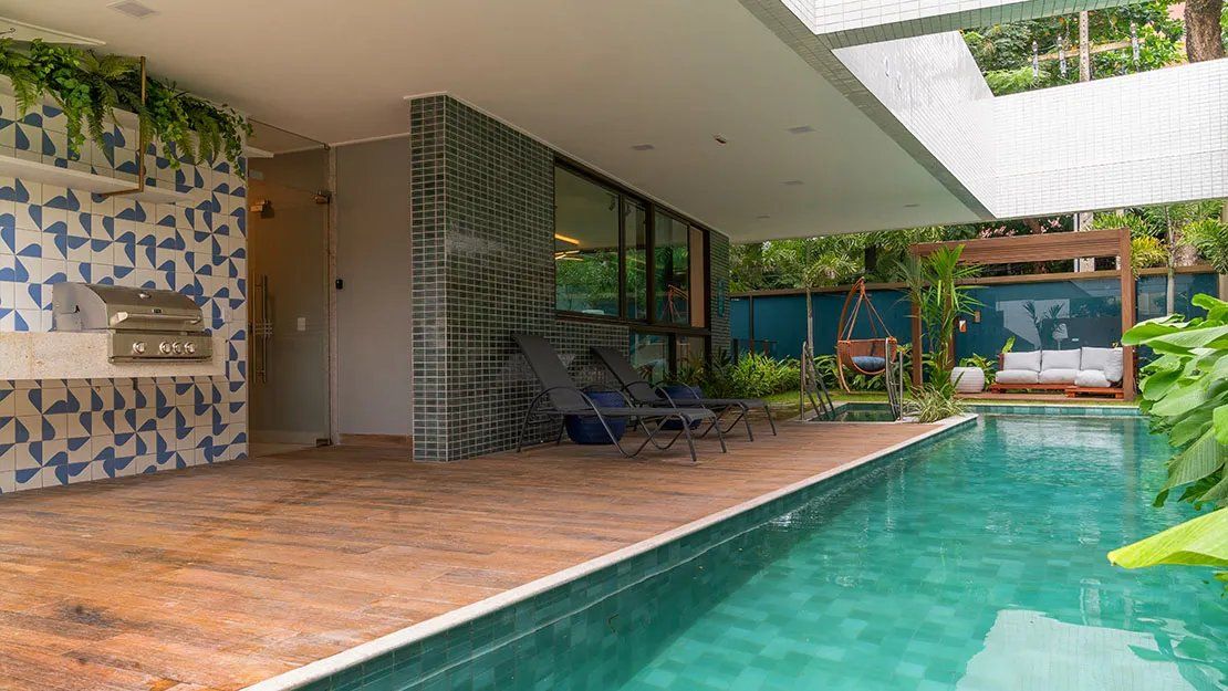 Uma área moderna de piscina ao ar livre com churrasqueira integrada, espreguiçadeiras e uma cadeira suspensa.