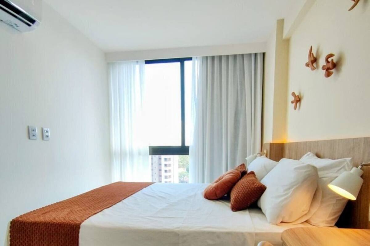 A hotel room with a bed, bedside table, and a view of the outside.