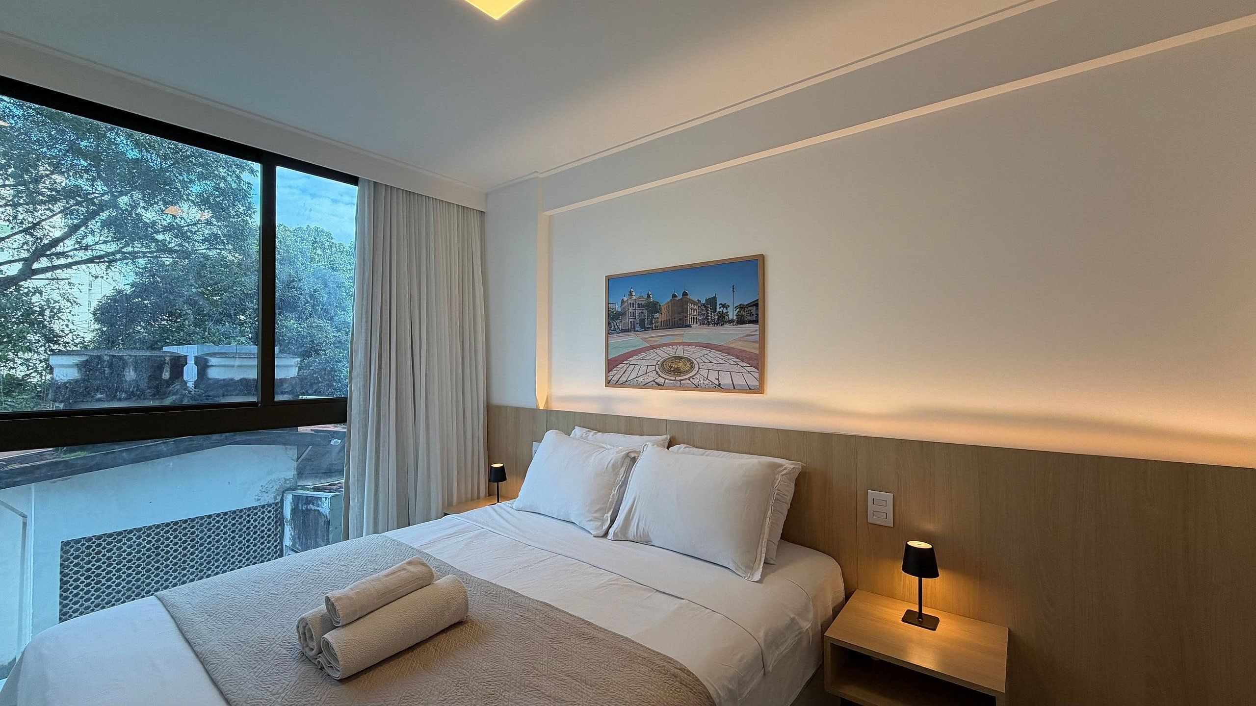 Habitación de hotel con una cama grande, vista a árboles por la ventana y un cuadro en la pared.