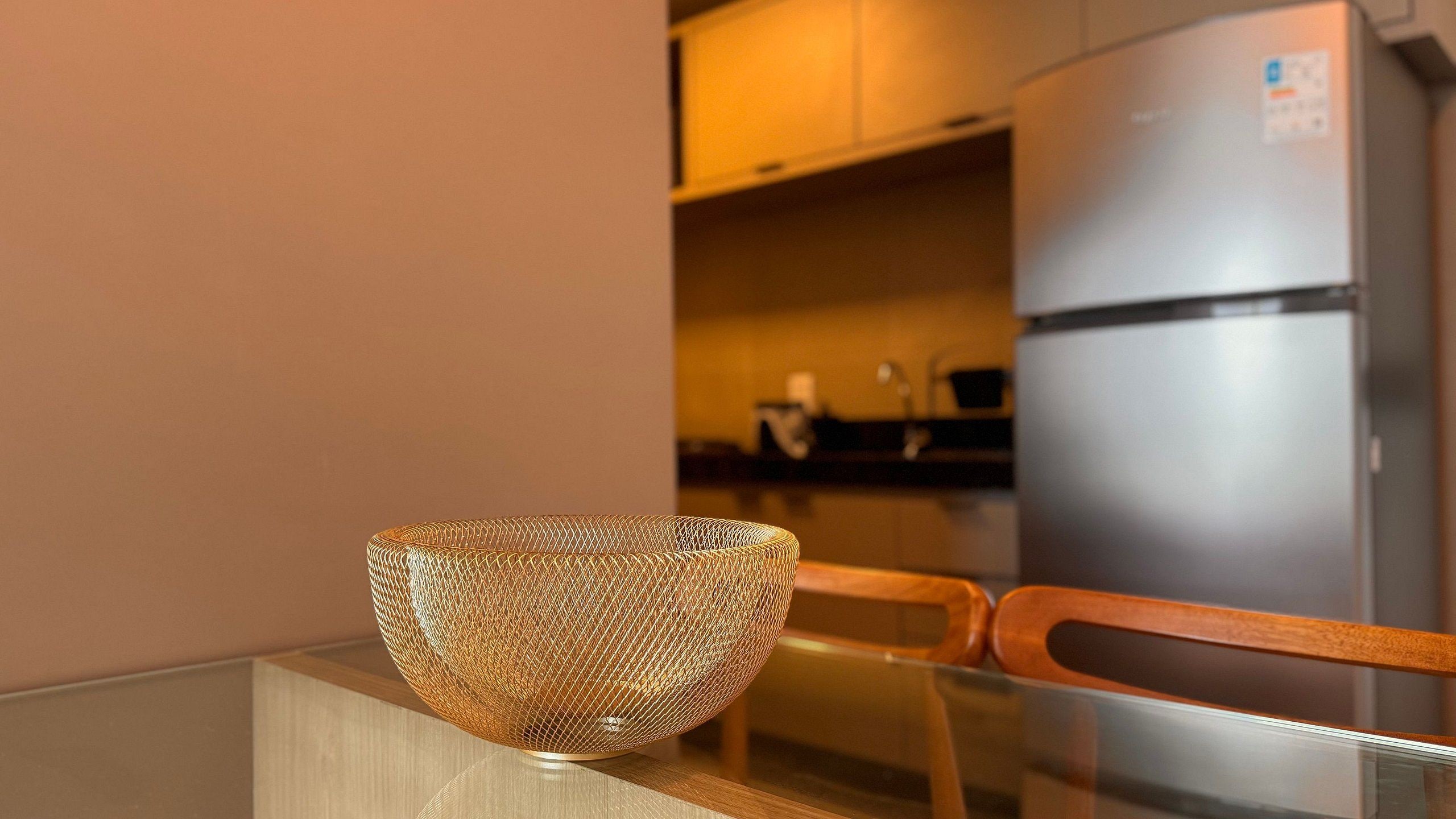 Una cocina moderna con un refrigerador de acero inoxidable, una silla de madera y una mesa de vidrio con una cesta de alambre.