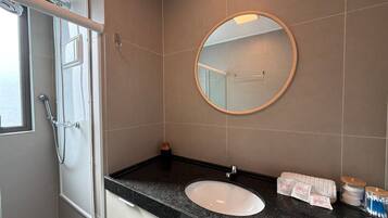 A bathroom with a white sink, a round mirror, and a shower door.