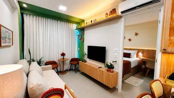 Quarto de hotel moderno com sofá, mesa de jantar, televisão e área de dormir separada.