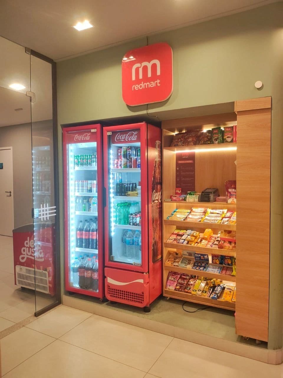 A Redmart store with three Coca-Cola refrigerators and a variety of snacks and beverages on shelves.