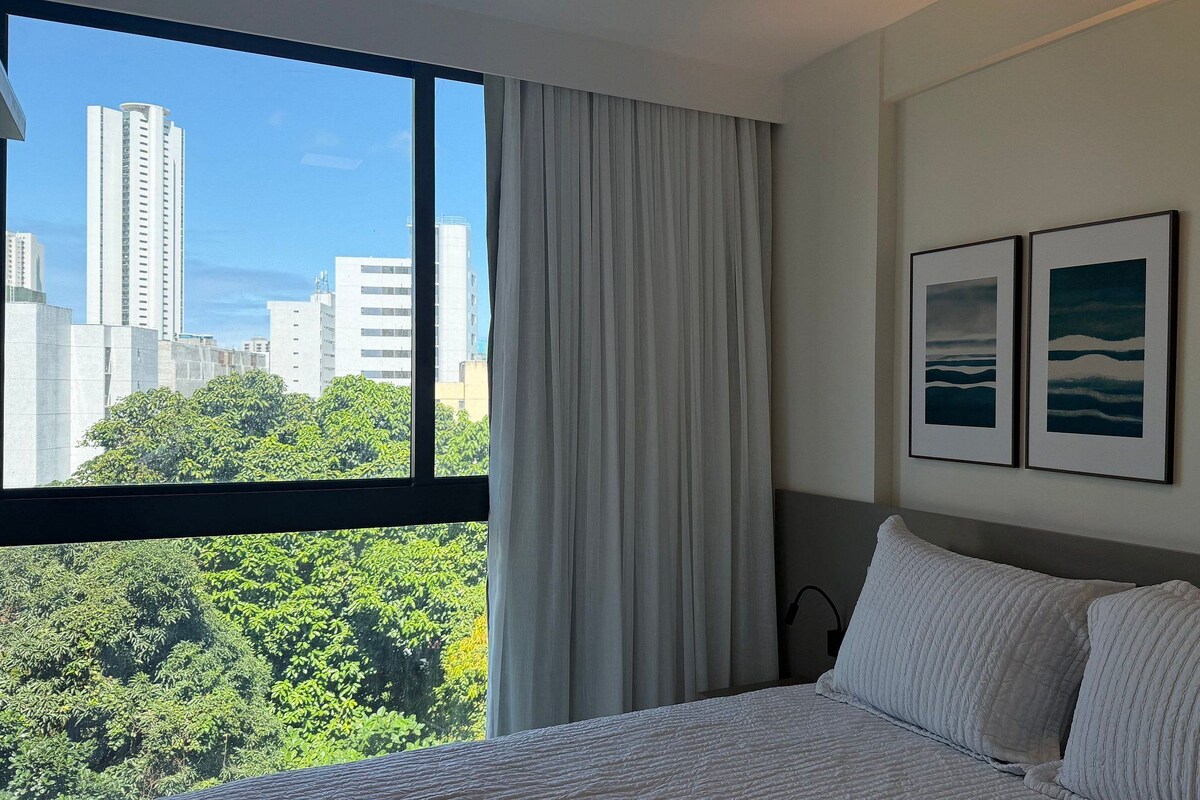 Une chambre d’hôtel avec une grande fenêtre, un lit et deux tableaux encadrés au mur.