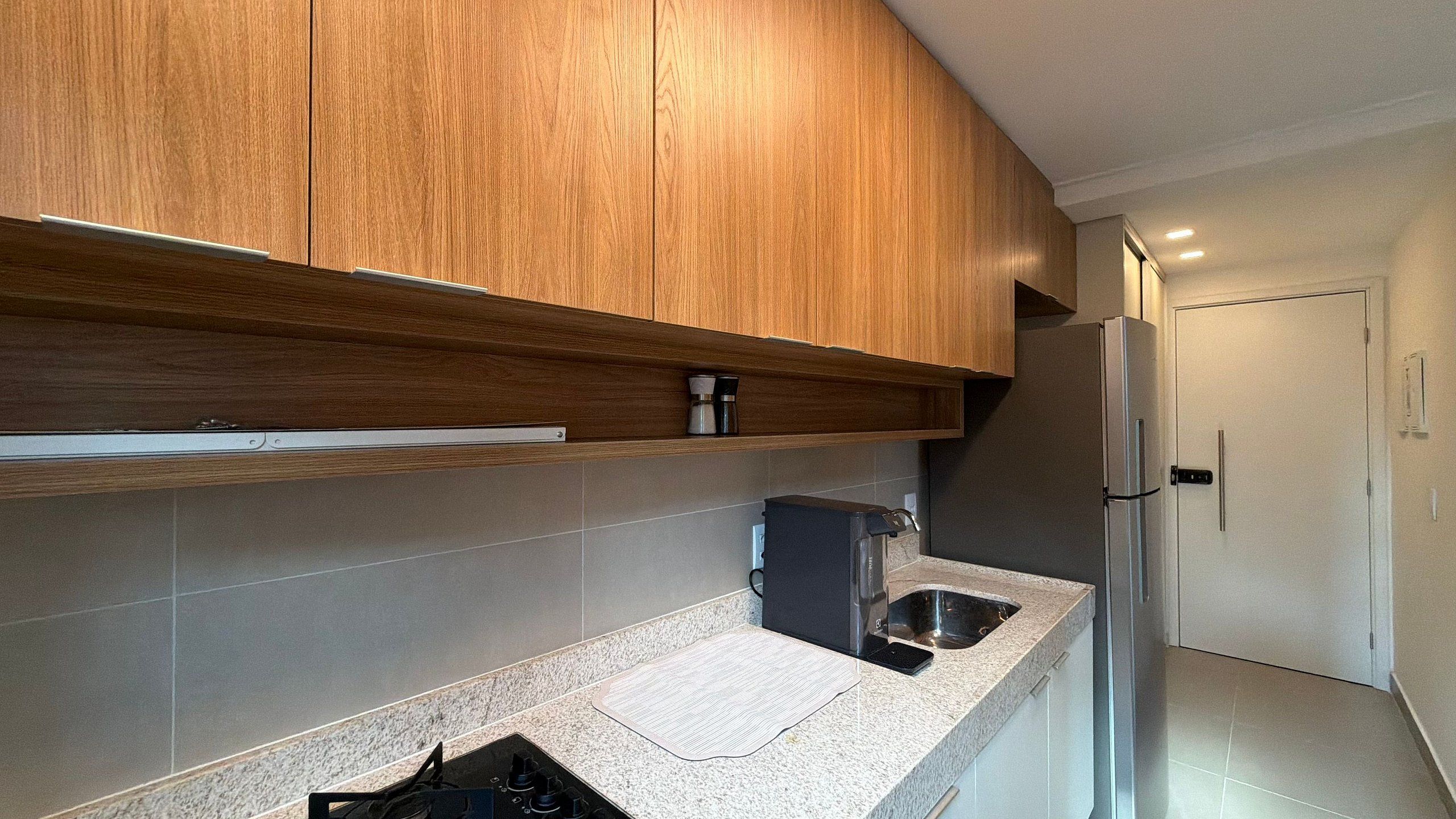 Una cocina moderna con armarios de madera, cafetera integrada y refrigerador de acero inoxidable.