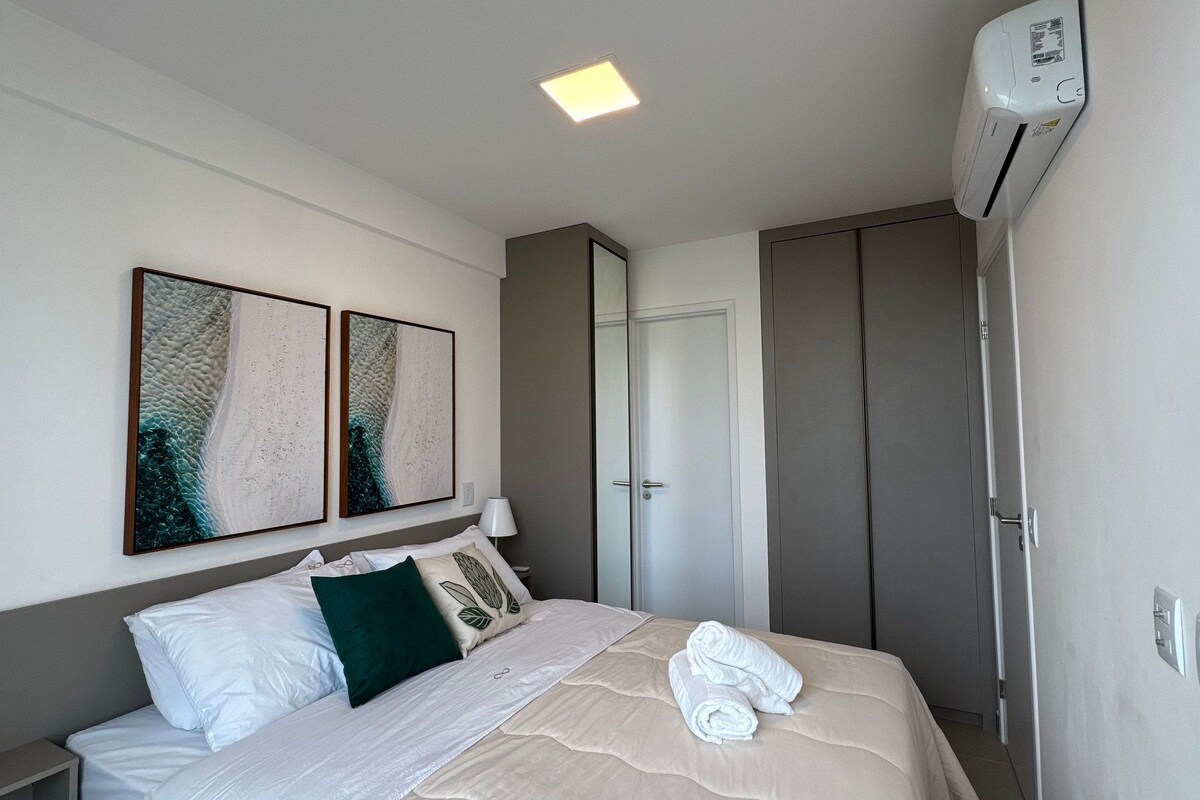 Ein Hotelzimmer mit einem Bett, zwei an der Wand befestigten Kunstwerken, einer Nachttischlampe, einem Kleiderschrank und einer Klimaanlage.